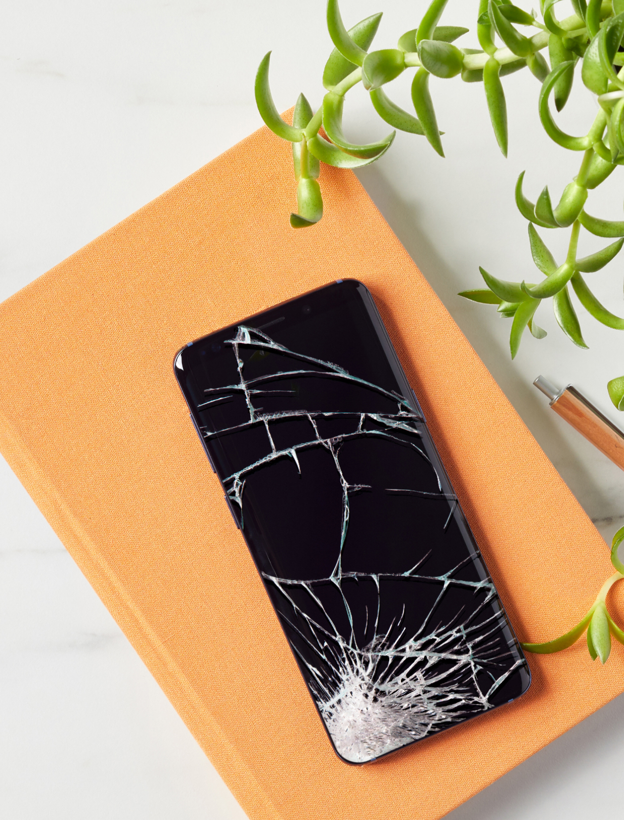 Smartphone with a cracked screen sits atop a desk