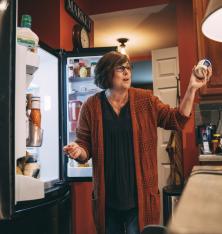 mother holding up mayo smiling in front of open fridge