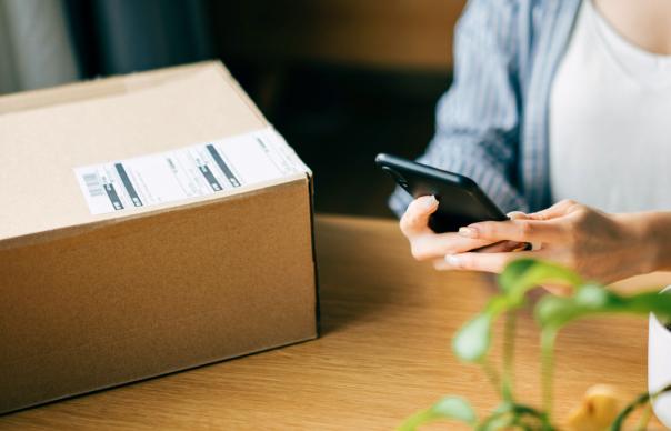 woman holding cell phone next top unopened package